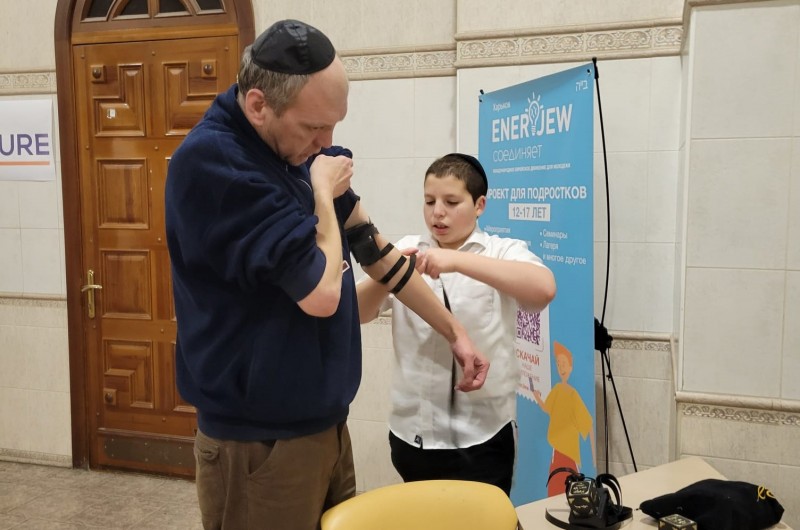 הת' יוסי מוסקוביץ' בנו של השליח הראשי בחרקוב הרב משה מוסקוביץ' מניח תפילין הבוקר, ליהודי שמסתתר בבית הכנסת, זאת בצל הקרבות וההפצצות בתוך העיר