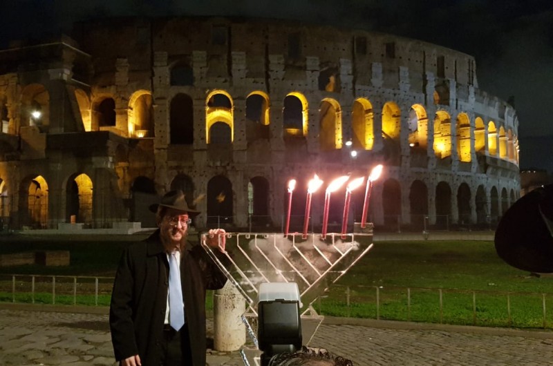 פרסומי ניסא באיטליה: הרב מנחם לאזאר, משליחי הרבי ברומא, מדליק נרות חנוכה בחנוכיית קרח על רקע מבנה הקוליסיאום המפורסם