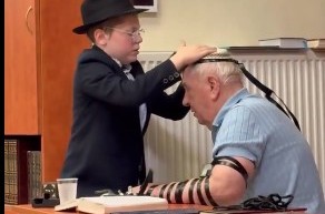 לרגל הנחת התפילין שלו ולקראת הבר-מצווה: התמים יונה סטמבלר, בן הרב שלום בער סטמבלר - שליח הרבי בוורשא שבפולין, מזכה יהודי בן 80 בהנחת תפילין 