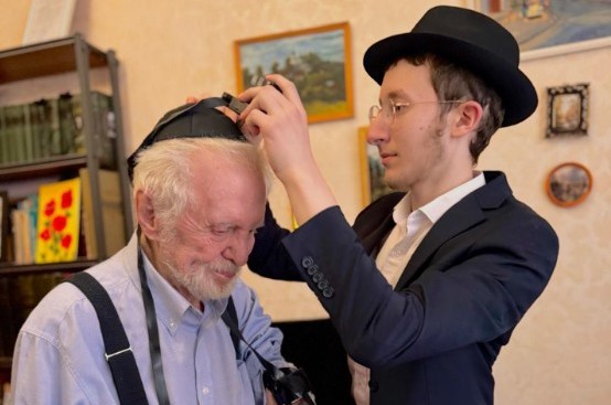 בן השליח מקאזאן שברוסיה, הרב יצחק גורליק, מניח תפילין לי. שפירא יהודי מהקהילה שחוגג היום יומולדת 100